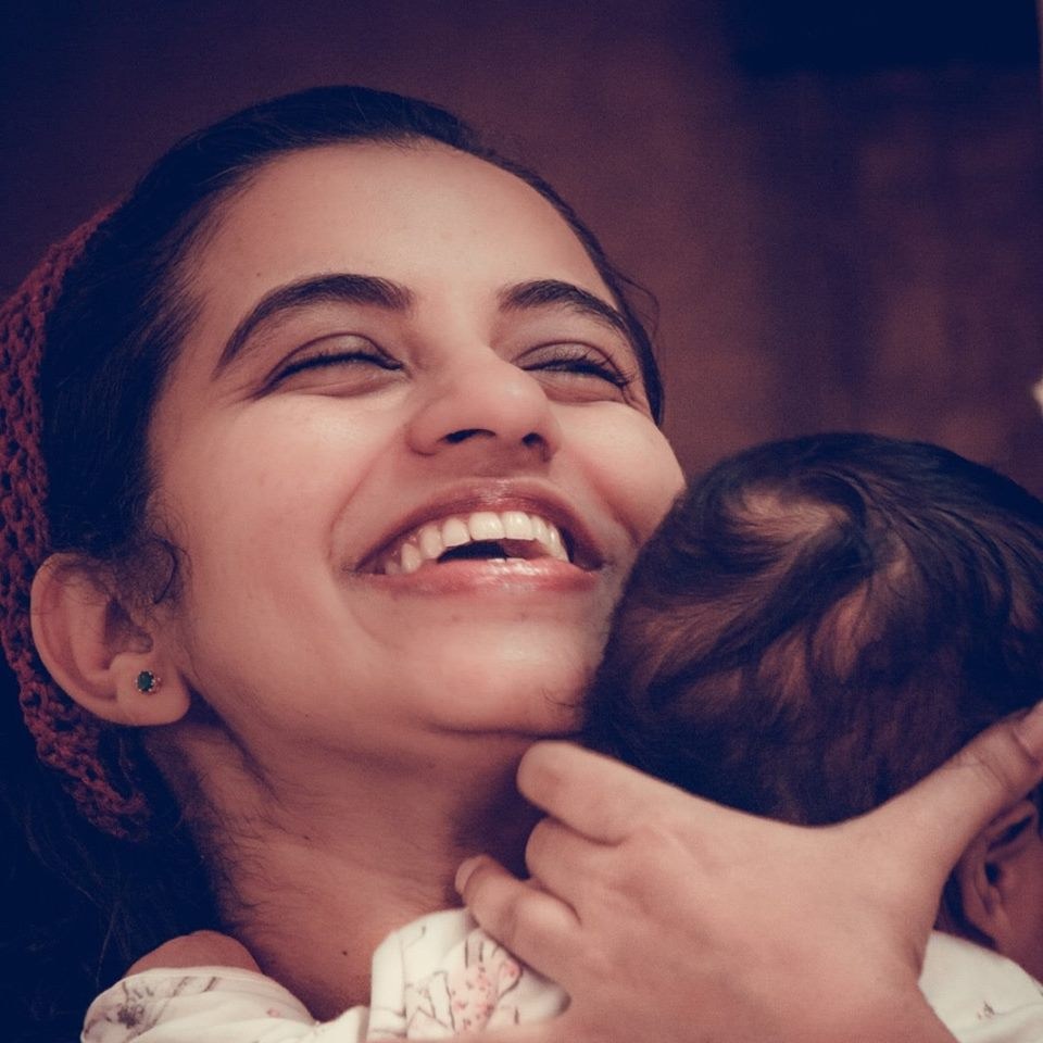 A young mother laughing with her baby in her arms